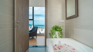 A modern bathroom with a bathtub, a view of the city, and a balcony with a chair. - Areca Hotel Nha Trang (Nha Trang)