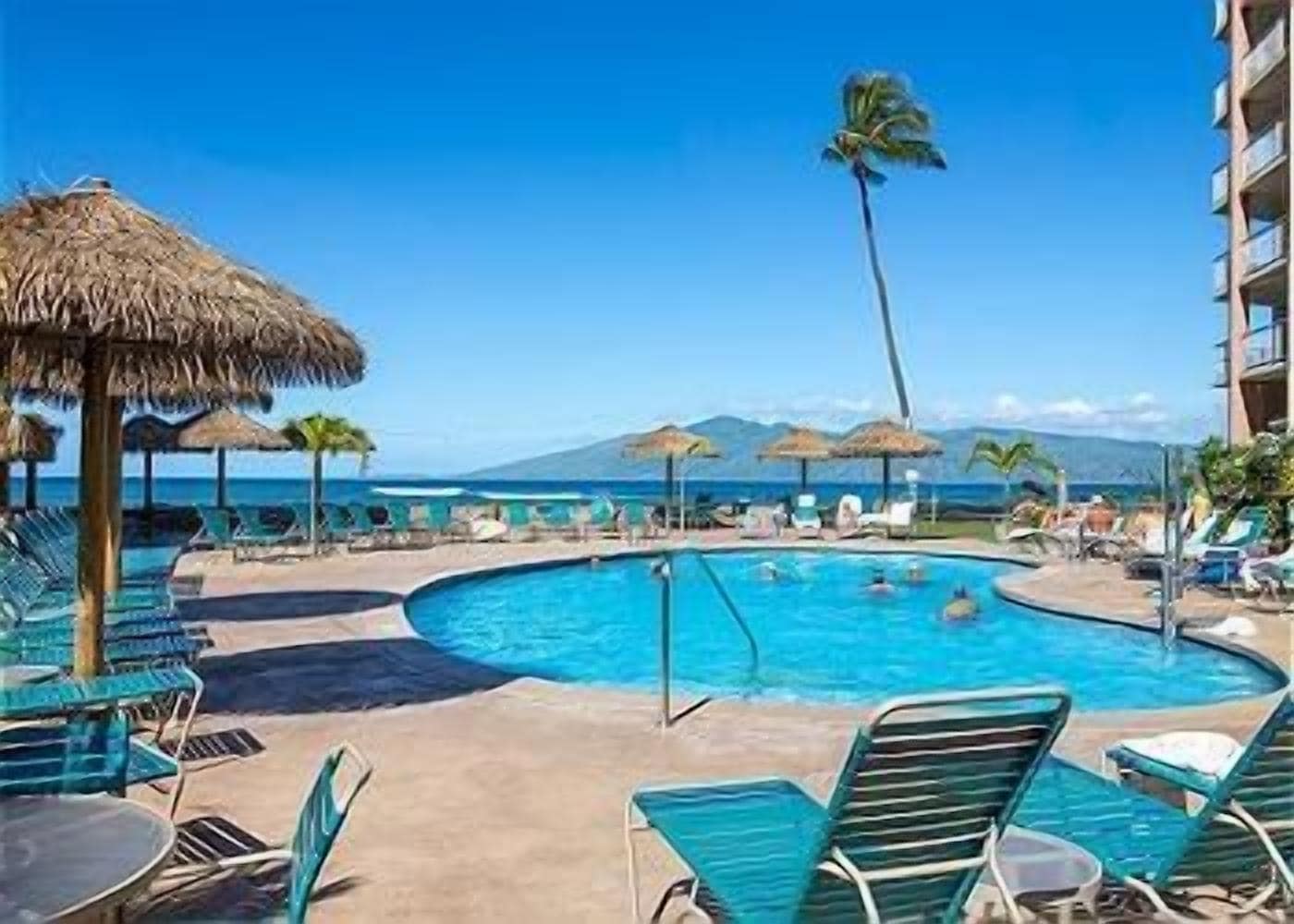Área de piscina com espreguiçadeiras e guarda-sóis, com vista para um corpo d'água e montanhas.