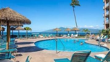 Área de piscina com espreguiçadeiras e guarda-sóis, com vista para um corpo d'água e montanhas.