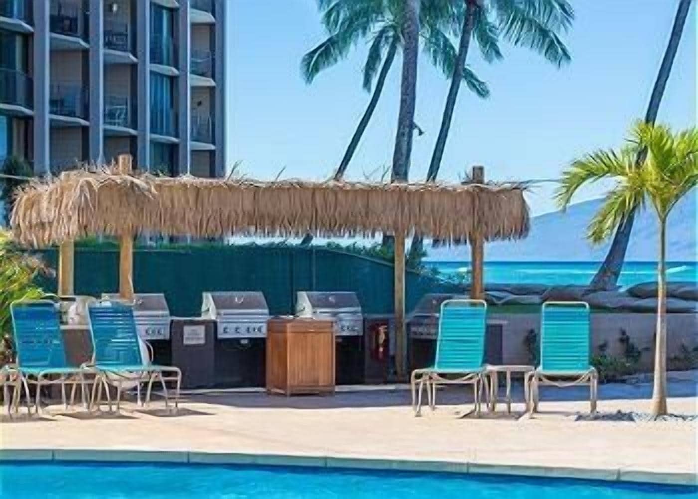Un espace aménagé au bord de la piscine, avec un barbecue, des chaises longues et une vue sur l’océan.