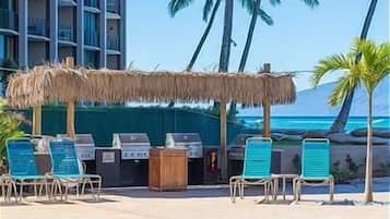Un espace aménagé au bord de la piscine, avec un barbecue, des chaises longues et une vue sur l’océan.