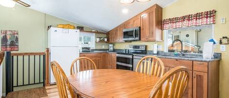 Una cocina con armarios de madera, microondas, refrigerador y una mesa de comedor con sillas.