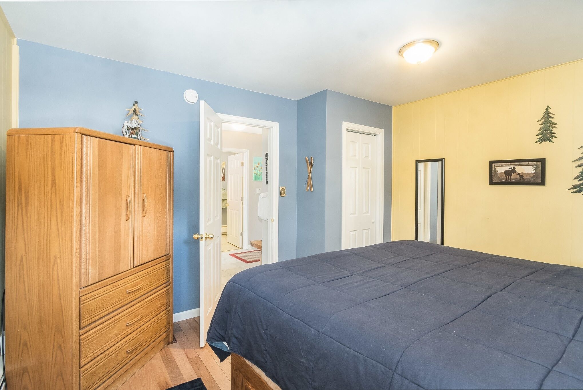 A bedroom with a bed, wooden wardrobe, and a door leading to another room.