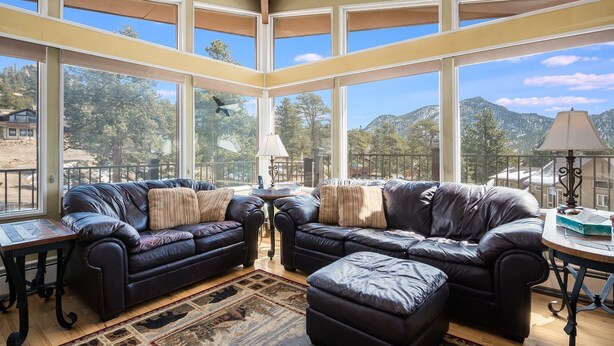 A spacious living room with a large window overlooking a mountainous landscape, furnished with leather sofas and a small table. - Starlight In The Rockies Ev #3172 3 Bedroom Home by RedAwning (Estes Park)