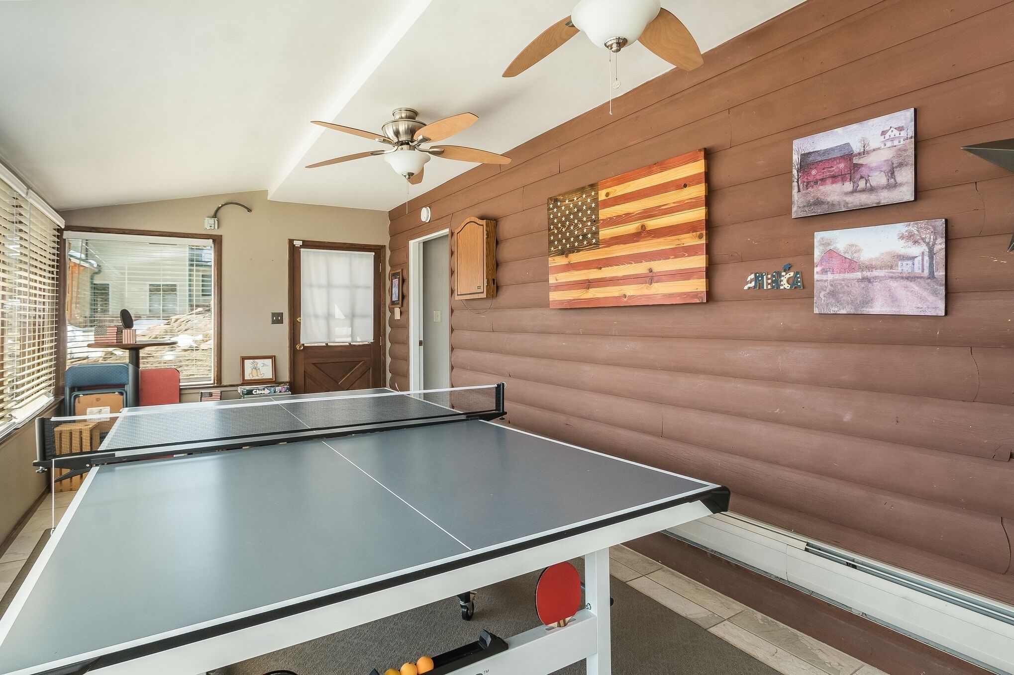 Una mesa de ping pong en una habitación con paredes de madera, ventiladores de techo y cuadros enmarcados.