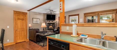 A kitchen with a dishwasher, wooden cabinets, a stone fireplace, and a large window.