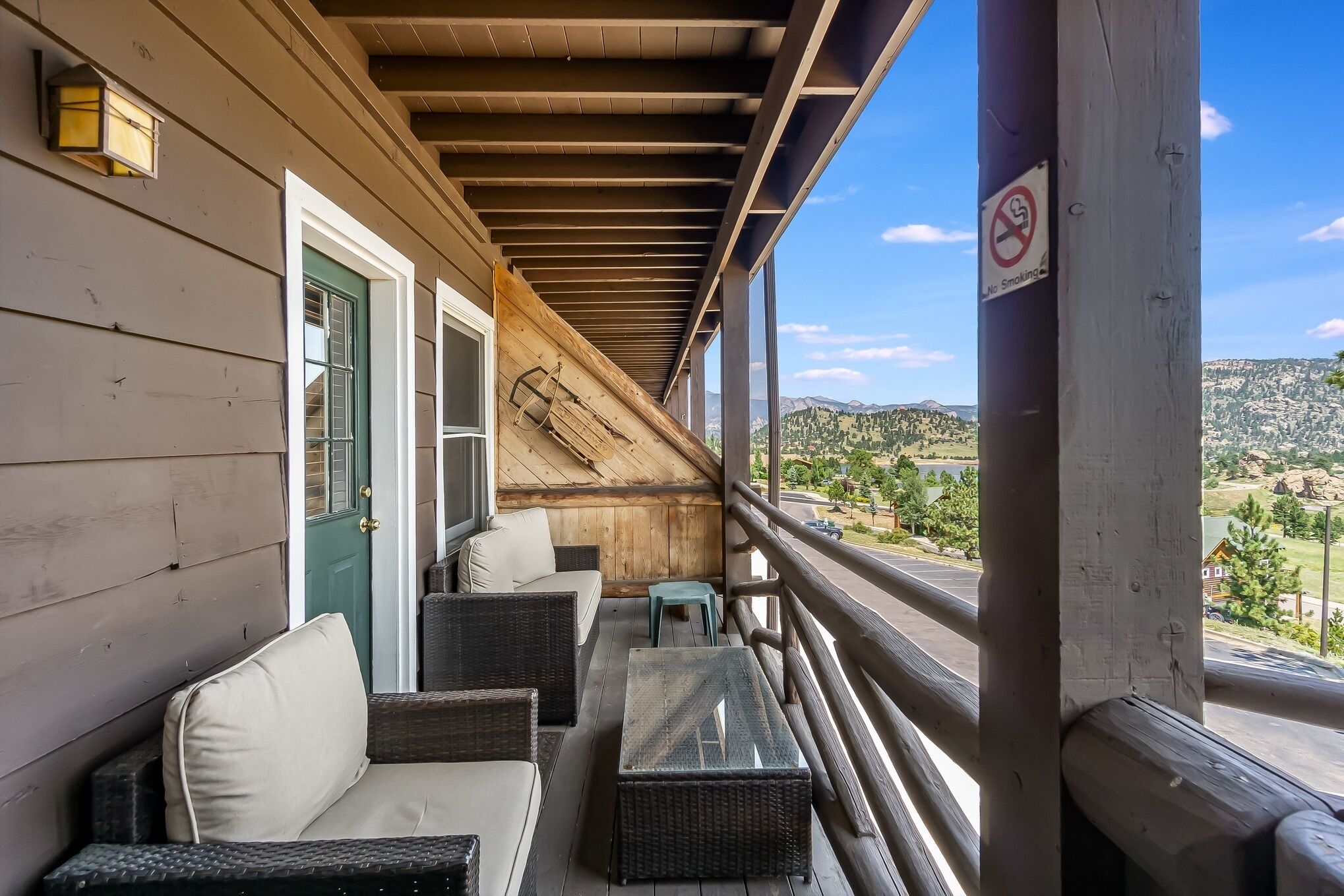Un balcon agrémenté de meubles en osier, d’une table en verre et offrant une vue sur une porte verte et un escalier en bois.
