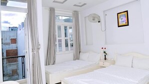 A hotel room with two beds, a balcony, a window with curtains, a bedside table with a lamp, and a picture on the wall. - Thanh Cuong Hotel (Nha Trang)
