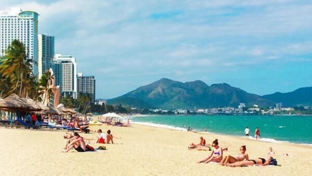 A beach with people sunbathing, palm trees, and a mountain in the background. - Thanh Cuong Hotel (Nha Trang)