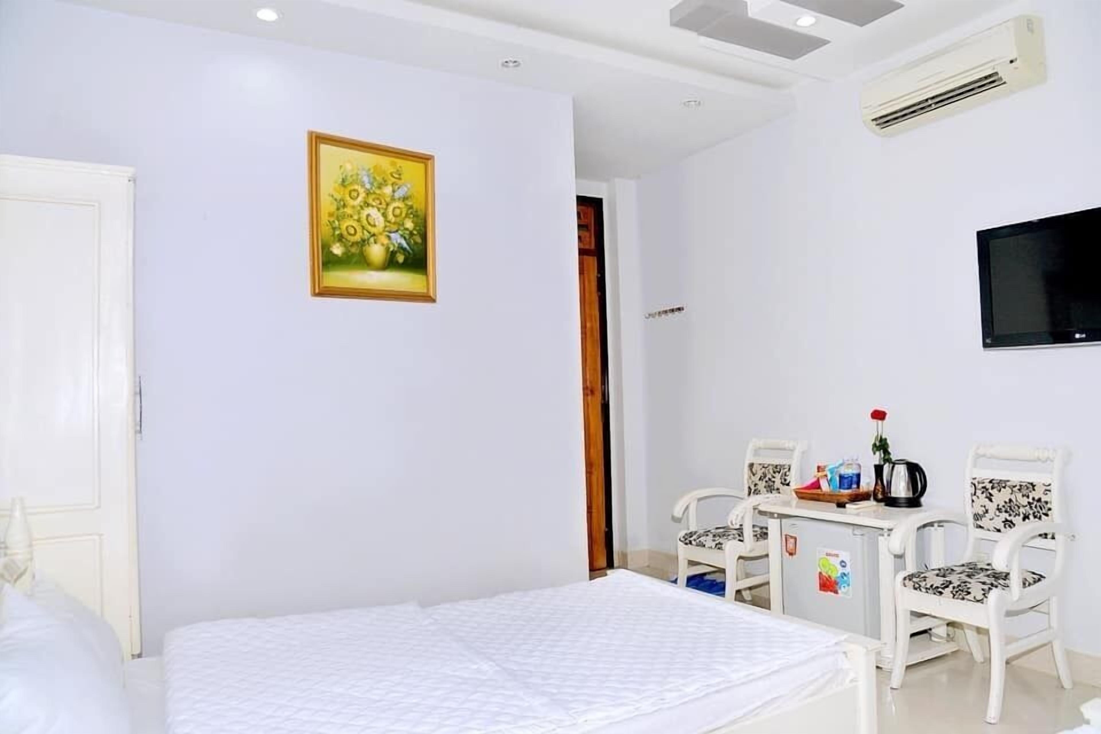 A bedroom with a bed, a TV, a small table with chairs, and a painting on the wall.
