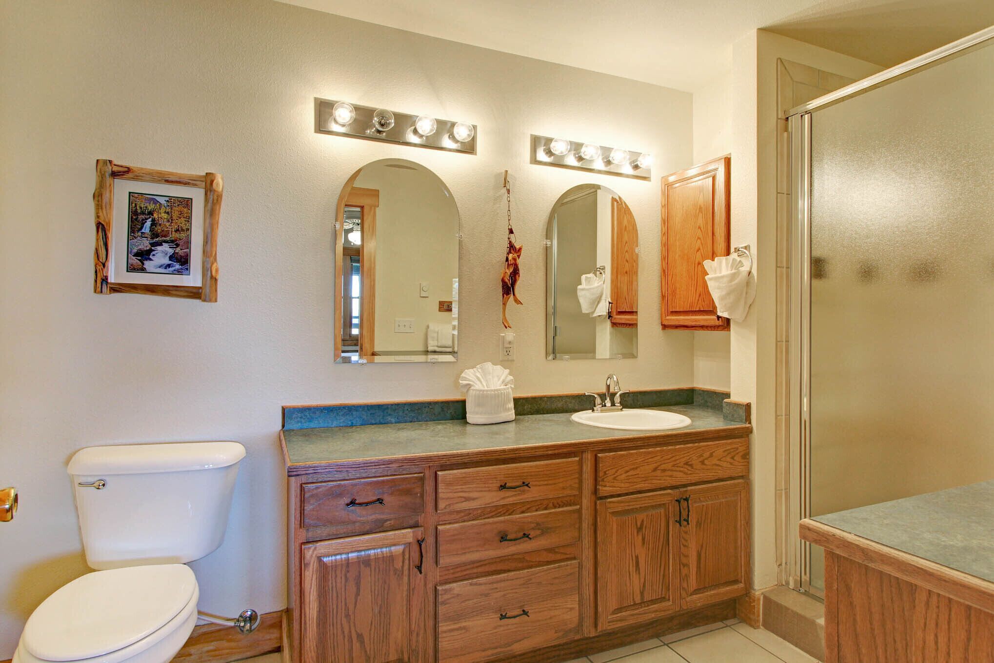 Un baño con inodoro, tocador de madera con cajones, lavabo y espejo.