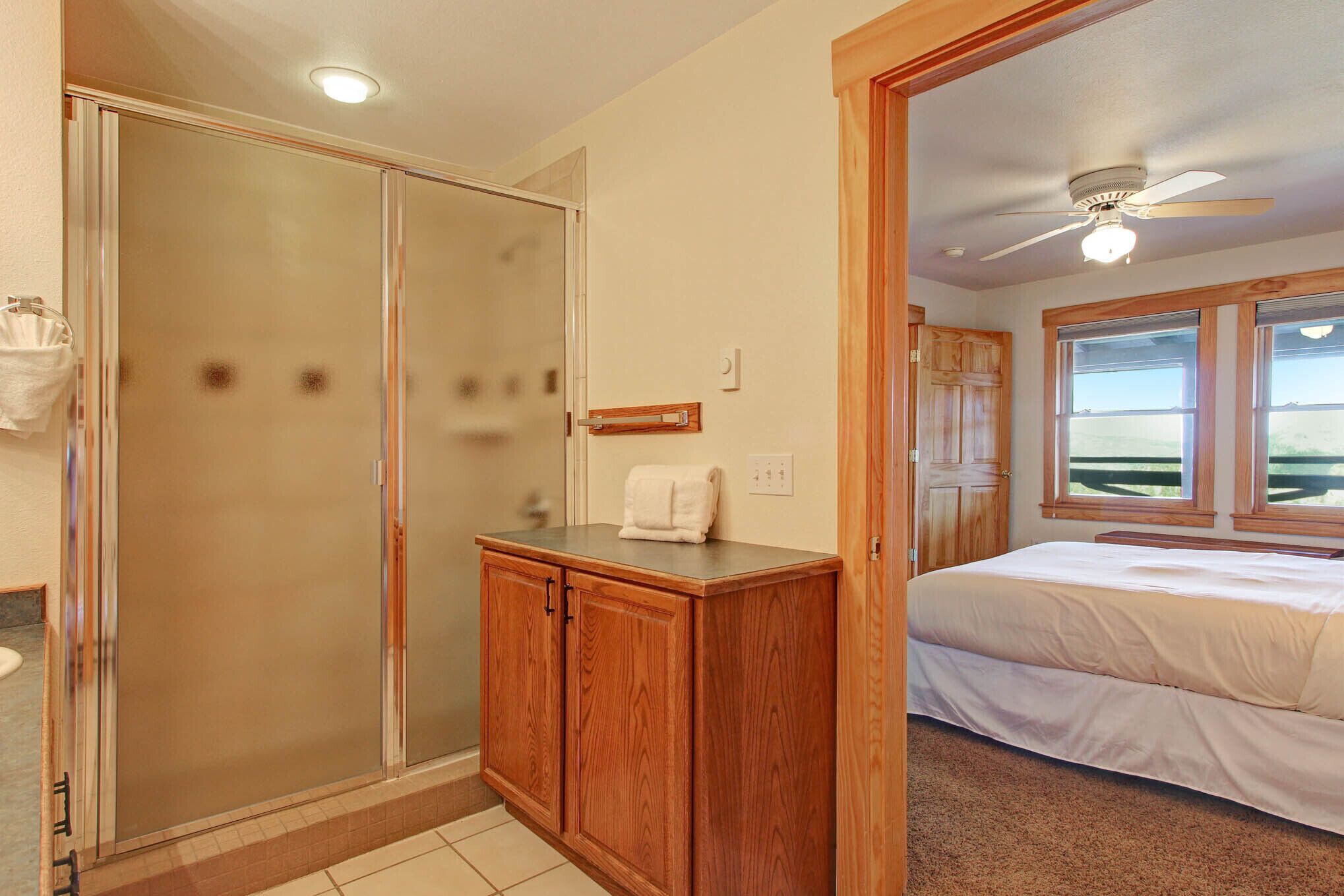 A bedroom with a bed, a wooden cabinet, a shower, and a window with a view.