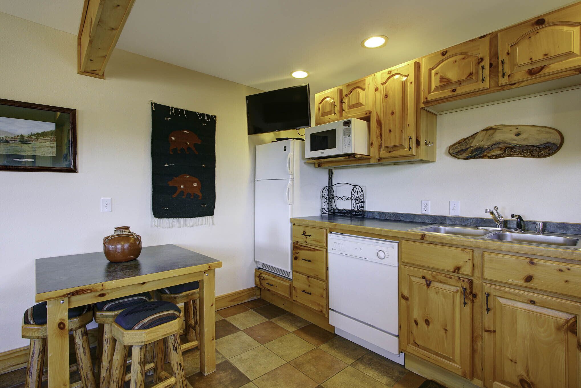 Une cuisine avec des meubles de rangement en bois, un four à micro-ondes, un réfrigérateur, un évier et une table avec des tabourets.