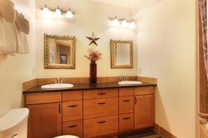 Un baño con dos lavabos, un mueble de tocador con cajones, un inodoro e iluminación empotrada.