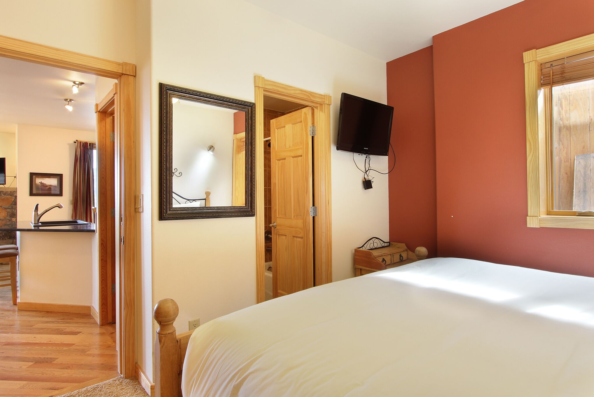 Un dormitorio con una cama, una puerta de madera, un televisor y un espejo.