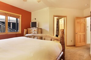 Un dormitorio con una cama, un televisor sobre un aparador de madera y una puerta de madera.
