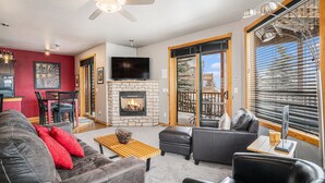 A modern living room with a stone fireplace, leather sofas, a wooden coffee table, and a television. - Nakai Peak 41b 2 Bedroom Condo by RedAwning (Estes Park)