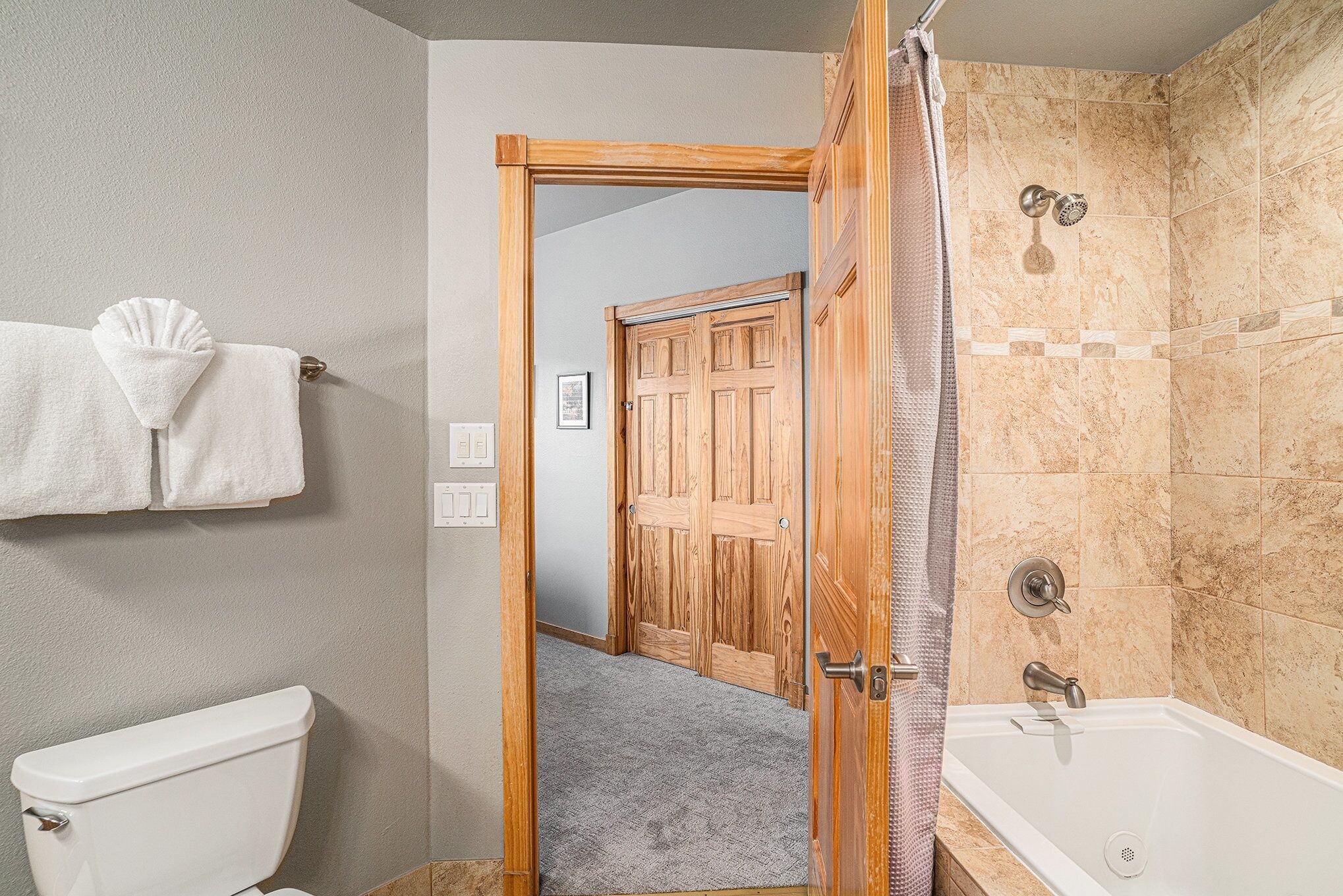 A bathroom with a toilet, a shower with a glass door, and a wooden door leading to another room.