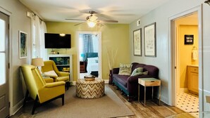 Ein Wohnzimmer mit einem gelben Sessel, einem violetten Sofa, einem Couchtisch, einem Deckenventilator und einem Fernseher.