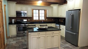 A kitchen with white cabinets, a stainless steel refrigerator, a double oven, a microwave, and a window above the sink.