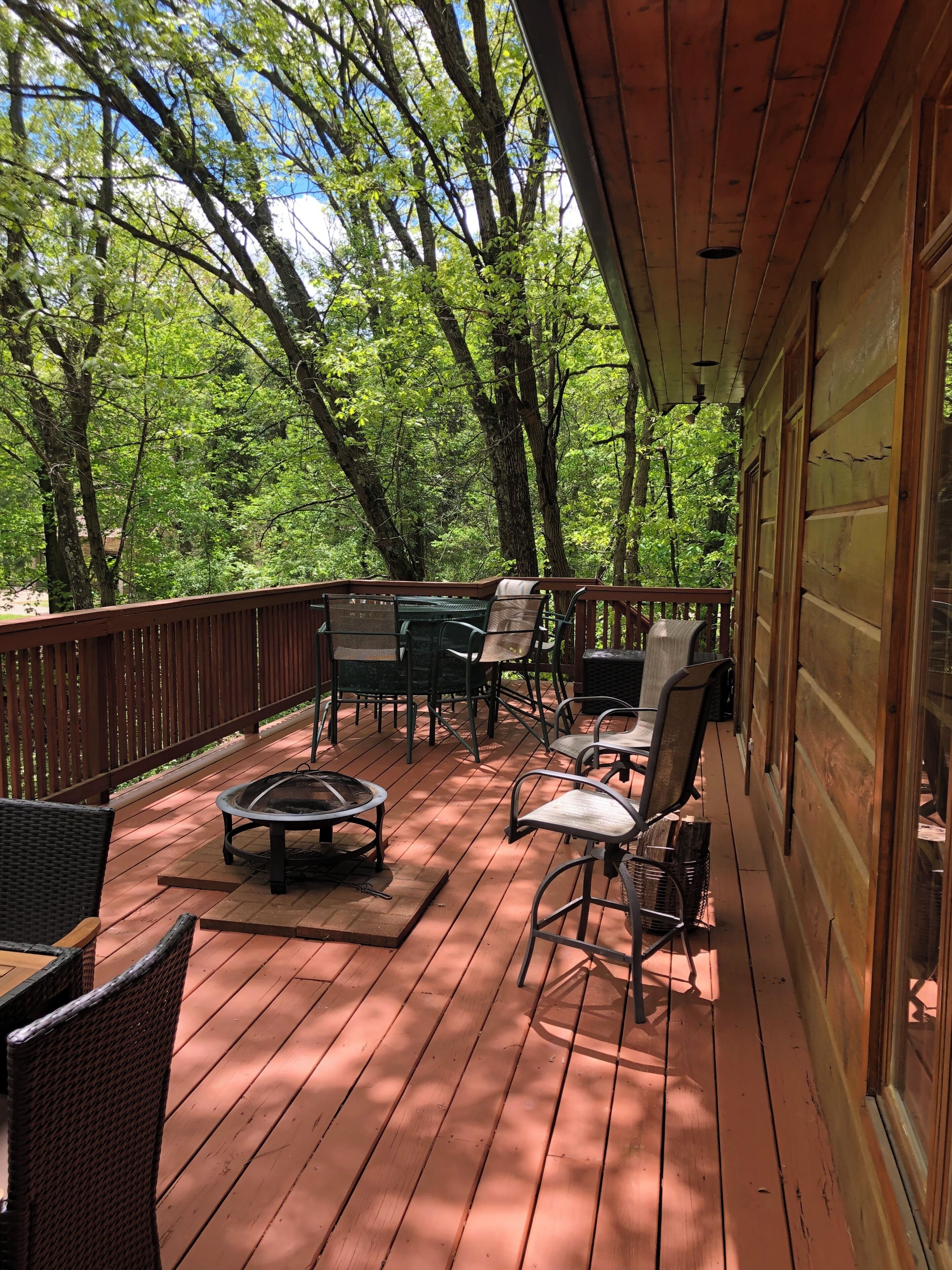 A wooden deck with outdoor furniture, including chairs and a table, overlooking a forested area.