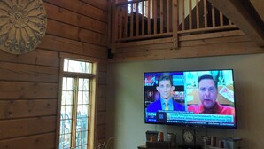 A wooden interior with a TV displaying news, a staircase, and a decorative wall piece.