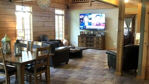A cozy living room with a wooden floor, a dining table with chairs, a sofa, and a television mounted on the wall.