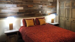 A bedroom with a wooden headboard, a red textured bedspread, two bedside lamps, and a nightstand with a drawer.