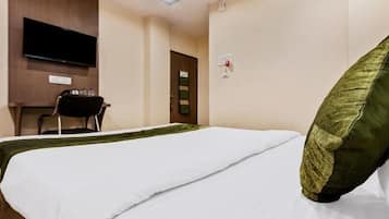 A hotel room with a bed, a TV mounted on the wall, a desk with a chair, and a door.
