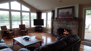 Una sala de estar con chimenea, televisor y amplios ventanales con vistas al agua.