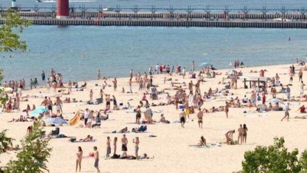 Una playa con un faro y un muelle al fondo.