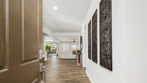 Un couloir avec un plancher en bois, un mur blanc orné d’œuvres d’art et une porte sur la gauche.