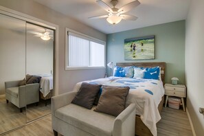 Ein Schlafzimmer mit einem Bett, einem Deckenventilator, einem Fenster, einem Gemälde, einem Nachttisch und einem Stuhl.