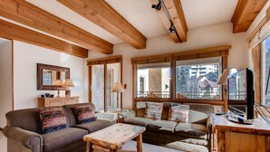 A cozy living room with wooden beams, a sofa set, a coffee table, and a television.