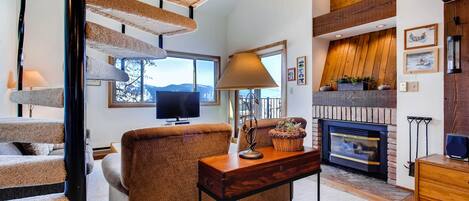 A spacious living room with a fireplace, a comfortable sofa, a wooden coffee table, and a modern staircase.