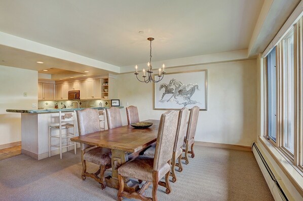 A dining room with a wooden table and chairs, a chandelier, and a kitchen in the background. - Amazing 2 Br Unit In Beaver Creek- Out Of A Western Movie 2 Bedroom Condo by RedAwning (Avon)