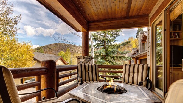 A wooden deck with a fire pit table and striped chairs, overlooking a mountainous landscape. - Excellent Location! Walk to Snow Park Lodge (Deer Valley)
