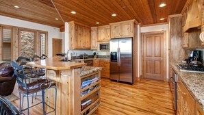 A kitchen with wooden cabinets, a stainless steel refrigerator, granite countertops, and a bar area with stools. - Excellent Location! Walk to Snow Park Lodge (Deer Valley)