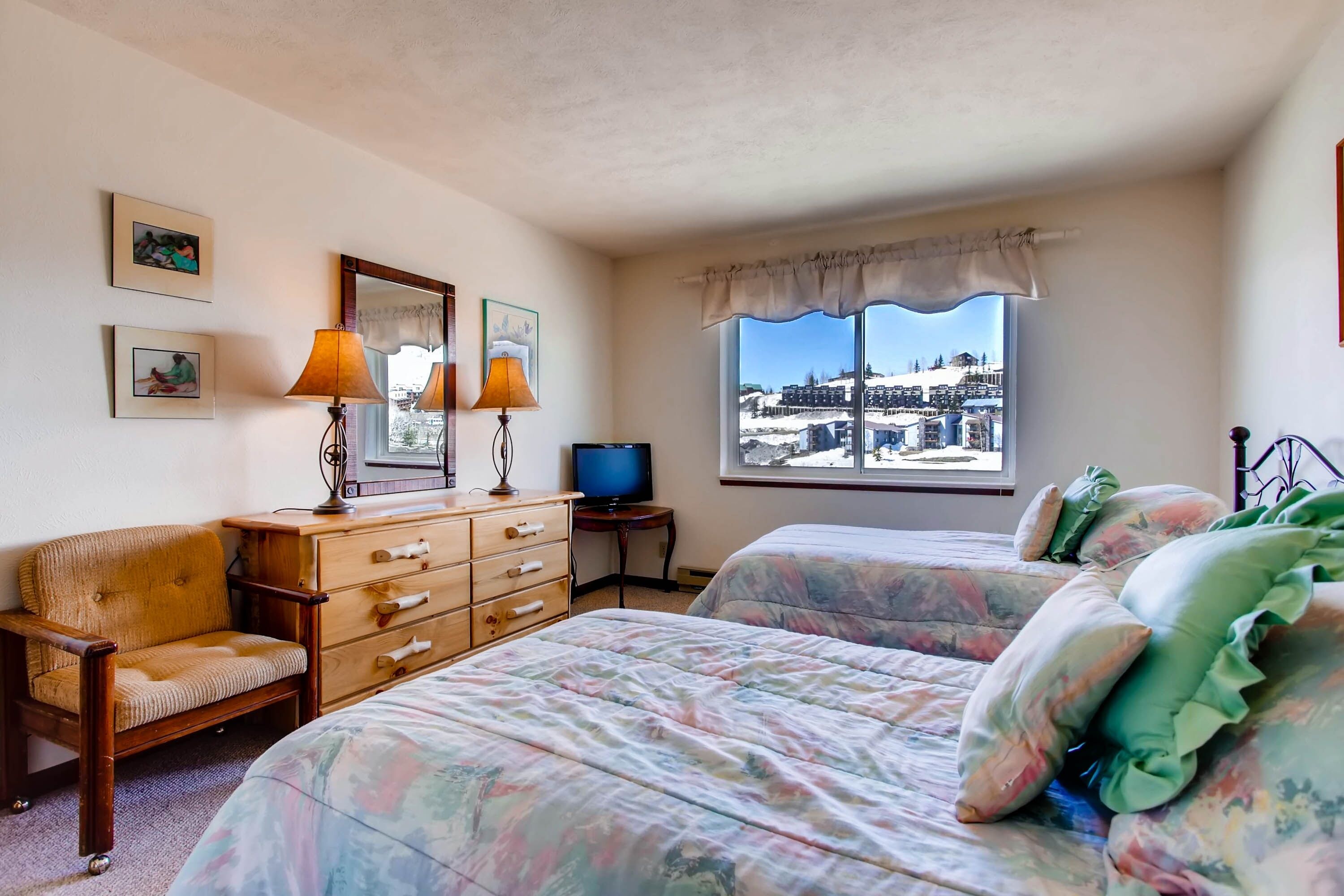 Un dormitorio con dos camas, un tocador, una silla, un televisor y una ventana con vista a la ciudad.