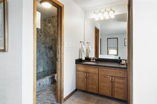 A bathroom with a stone shower, wooden cabinets, a sink with a mirror, and a light fixture above the mirror. - Recently Updated Plaza  3 Bedroom Condo - No Cleaning Fee! by RedAwning (Crested Butte)