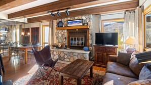 Een gezellige woonkamer met een stenen openhaard, een televisie en een eethoek met stoelen en een tafel.