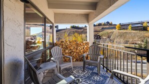 Een balkon met stoelen en een getextureerd vloerkleed, met uitzicht op een schilderachtig landschap met bomen en een gebouw.