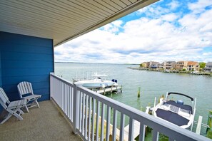 Ein Balkon mit zwei Adirondack-Stühlen, ein Steg mit einem Boot und Blick auf einen Hafen mit Gebäuden im Hintergrund.