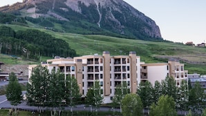 Ein mehrstöckiges Hotel mit modernem Design, gelegen in einer hügeligen Landschaft mit einem Berg im Hintergrund.