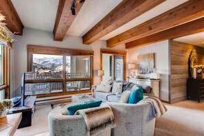 Un vaste salon doté d’une grande fenêtre offrant une vue sur les montagnes, de poutres en bois au plafond et d’un coin salon confortable avec une cheminée.