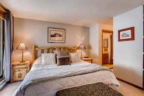 A neatly arranged bedroom with a large bed, two bedside tables with lamps, a wooden headboard, and a framed picture on the wall.