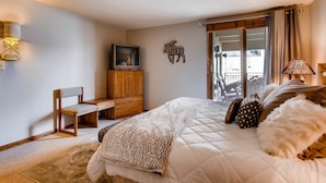Ein Schlafzimmer mit einem Bett, einem Holztisch, einem Fernseher und einem Balkon mit Vorhängen.