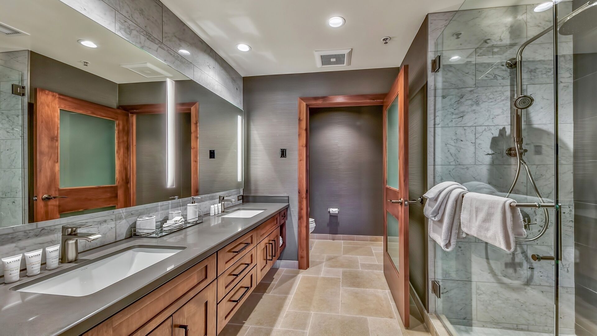 Une salle de bain moderne avec deux lavabos, un grand miroir et une douche à parois de verre.