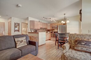 A modern kitchen with wooden cabinets, a central island, and a dining area with a wooden table and chairs. - Spacious  In The Heart Of Breckenridge Studio Condo by RedAwning (Breckenridge)