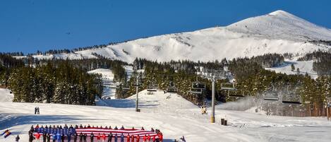 A ski resort with a mountain backdrop, ski lifts, and a group of people holding a large flag.